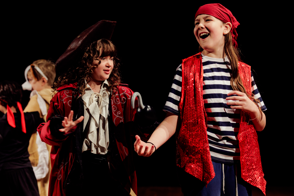 Young people on stage, dressed up as pirates: stripey tops, bandanas, and a hook